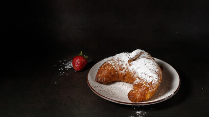 Fresh baked butter croissant  with sugar powder on white ceramic plate with strawberry  on vintage brown background.