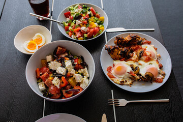 Cooked scrambled eggs with salad. Shakshuka serving on the summer terrace. Breakfast outside. Fried eggs on the summer terrace for breakfast. Breakfast is served on the table for two. Food day. Greek 
