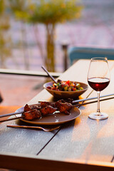 Fried meat on a skewer.Shish kebab on a plate.Skewer with a kebab and a glass of wine.Dinner on the terrace with wine and meat.Fried meat for dinner.Meat.Covered dinner.Delicious food.Summer