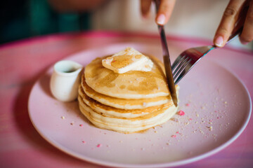 Young woman cuts piece from stack of sweet pancakes with soft cheese or butter drenched in honey. Sweet desserts.Concept of proper nutrition. Homemade food. Enjoy desserts. Serene morning.