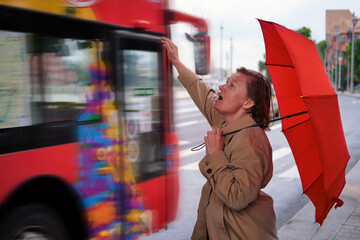 Adult woman with a red umbrella in the rain at the tourist bus