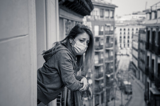 Lonely Woman With Face Mask In Quarantine Feeling Sad And Hopeless Looking Outside In Home Balcony