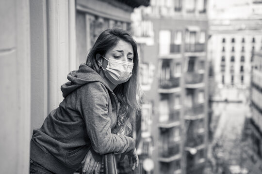 Lonely Woman With Face Mask In Quarantine Feeling Sad And Hopeless Looking Outside In Home Balcony