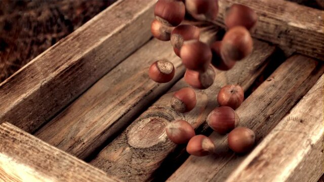 Super slow motion hazelnuts fall on a wooden tray. Against a dark background. Filmed on a high-speed camera at 1000 fps.