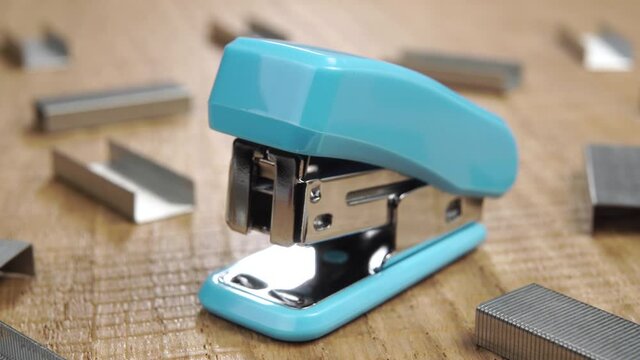 Office stapler with staples on a wooden textured table. Macro shot. Blue plastic handle. Desktop tool. Dolly shot