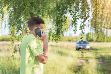 Man talking on the phone in front of the car in the park.