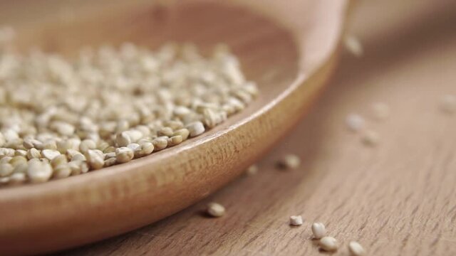 Grains of raw white quinoa fill a wooden spoon in slow motion. Macro shot. Super healthy gluten free food concept