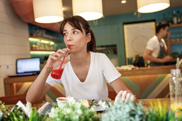 Teenage girl sitting in fast food restaurant eating burger and drinks fresh organic juice.	
