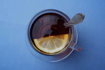 a glass of tea with lemon and two pieces of sugar stands on a glass saucer on a blue background