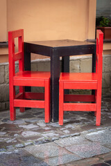 Fototapeta na wymiar Outdoor cafe furniture. Empty wooden table and red chairs near restaurant window. Sidewalk cafe. Big city life. Street life. Vintage style of furniture. Seat and table on the street. No people in cafe