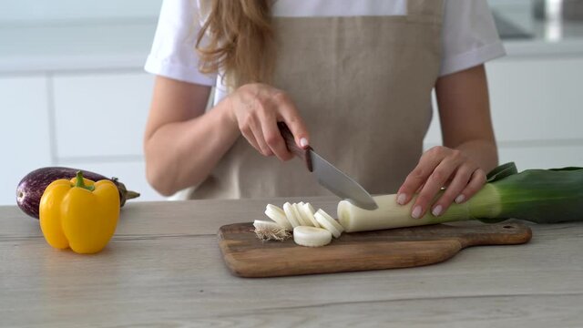 Women's hands cut fresh leeks on the wooden cutting board. Cooking at home.