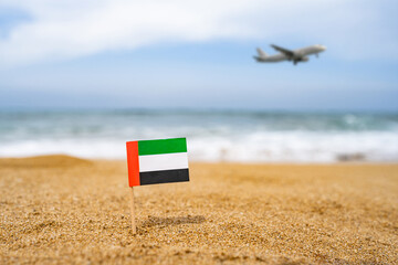 Flag of United Arab Emirates in the form of a toothpick in the sand of beach opposite sea wave with...