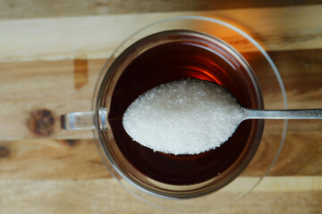 someone adds a spoonful of sugar to a glass of tea