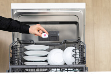 Housewife inserting detergent tablet into dishwasher slot
