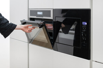 Woman holding electric ovens door in kitchen