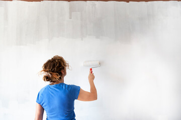 Woman painting new apartment walls in color white with paint roller. Renovating house.