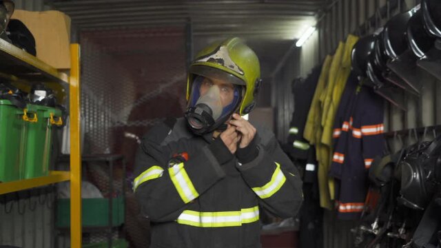 A caucasian firefighter or fireman with uniform and mask, wearing safety helmet in protection gear storage. An emergency accident rescue. People. Hero. Service job