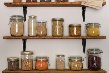 Open pantry wooden shelves with glass storage containers filled with grains and legumes .