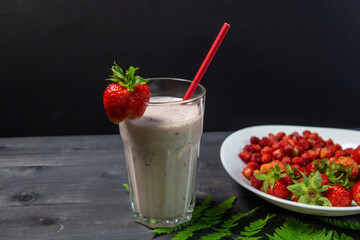 strawberry smoothie in glass on black background with berries in plate