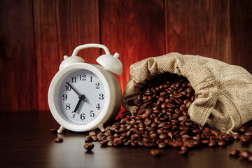 A white alarm clock and coffee beans in a bag on wooden table