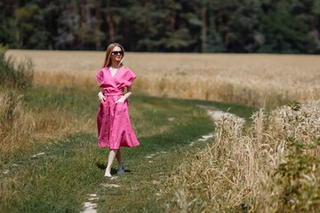 Fototapeta premium A beautiful young woman is walking in a wheat field