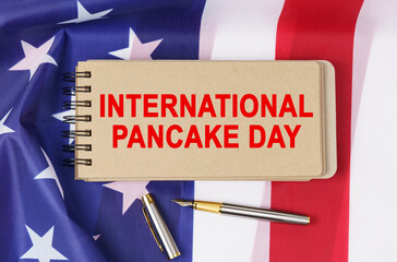 Fototapeta na wymiar Against the background of the US flag lies cardboard with the inscription - INTERNATIONAL PANCAKE DAY