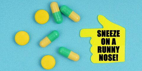 On a blue background, there are pills and a hand-sticker with the inscription - Sneeze on a runny nose
