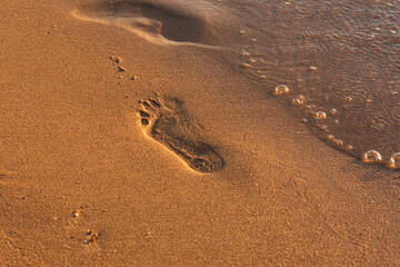 Footprints of the golden sand beach. Small waves roll up on the shore and wash away the tracks. The man walked along the beach. Summer textured background. The concept of rest, relaxation, privacy.