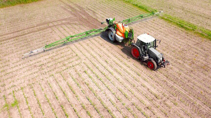 Traktor mit Feldspritze versprüht Pestizide auf Maisacker, Landwirtschaft aus der Vogelperspektive