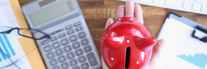 Pig piggy bank on female hand next to calculator and documents on table