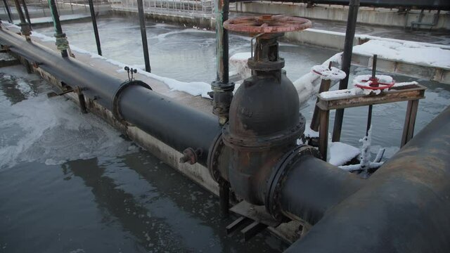 Pipe with red round levers near basin with swirling wastewater at contemporary treatment plant at sunset light close view