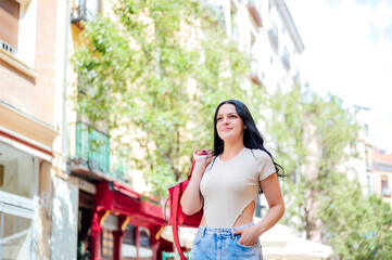 Smiling beautiful young woman with her hand in her pocket, standing on the street while looking away on a sunny day