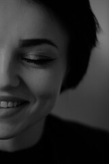 A happy young girl in a black leather jacket and short hair is sitting at a table. Black and white portrait of a smiling woman	