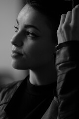 A happy young girl in a black leather jacket and short hair is sitting at a table. Black and white portrait of a smiling woman	