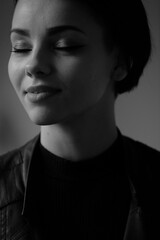 A happy young girl in a black leather jacket and short hair is sitting at a table. Black and white portrait of a smiling woman	