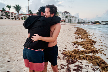 portrait of homosexual couple of two men hugging in the middle of the beach of cancun in the mayan rivera, mexico, in the middle of the sargasso and the sunset
