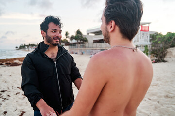 portrait of young latin man looking at his homosexual partner in the middle of the beach in cancun...
