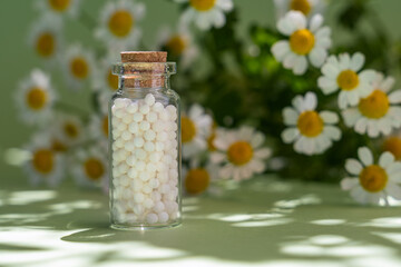 Classical homeopathy globules in vintage bottles on background of fresh chamomile flowers. Alternative homeopathy medicine herbs, healthcare and pills concept.