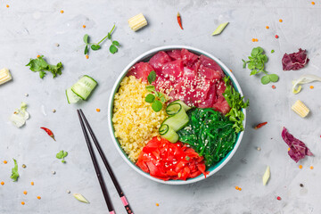 Hawaiian popular poke dish with tuna, bulgur and chuka seaweed. Vegetarian bowl with seafood and salad. Top view on a gray background with chopsticks , close-up,