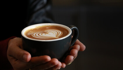 close up young woman hand hold and serve hot coffee cup with latte art heart shape