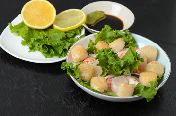 Fried scallop meat with boiled shrimps in a ceramic plate with lettuce, lemon, soy sauce and wasabi