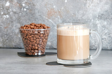 Cappuccino in a glass transparent large glass next to the coffee beans. Gray background.
