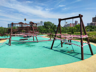 Closed outdoor child playground in sunny day in city park in Moscow, Russia. No children. Barricade tapes hangs on playground. Selective focus. Illness prevention theme.