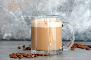 Cappuccino in a glass transparent large glass next to the coffee beans. Gray background.