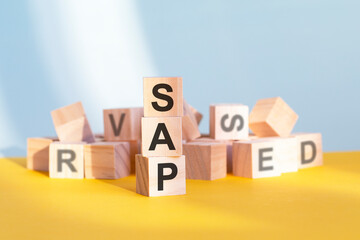 Obraz premium wooden cubes with letters sap arranged in a vertical pyramid, yellow background, reflection from the surface of the table, business concept