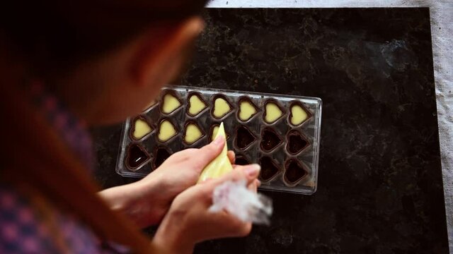 Top view video of a confectioner chocolatier filling chocolate molds with creamy filling to preparing delicious handmade pralines at home. World Chocolate Day. Cooking video lessons. Culinary Blog con