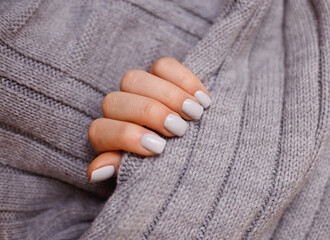 Fingers with gray manicure holding a texture. Modern style  Nail Polish.Shellac.Female hand with gray nail design. Woman hand on gray fabric. Trendy colours.Gray manicure nails with a grey scarf.