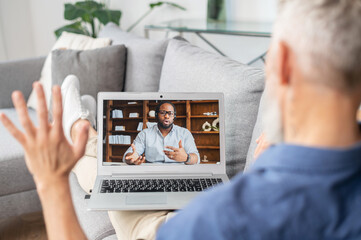Two diverse male colleagues talking on the distance via video connection. Senior grey haired man...