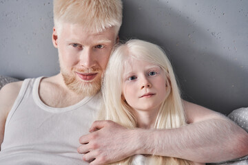 Man embracing his lovely blonde daughter while laying together at the bed