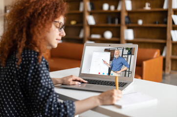 E-studying concept. Curly female student watching online educational webinar, listening a senior...